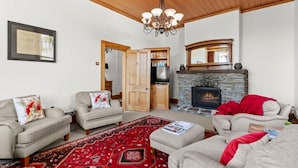 A living room with a fireplace, two sofas, a rug, and a wooden door leading to a kitchen. - Historic Stone Cottage Apt 1- spa - 3 min from town (Queenstown)