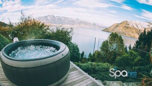 A hot tub on a wooden deck overlooking a lake with mountains in the background. - Remarkable View 3 bedroom - lake and mountain views (Queenstown)