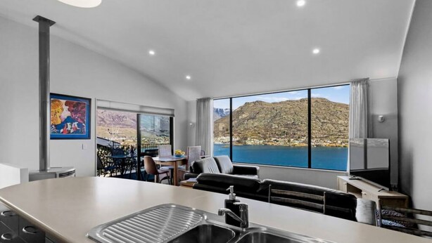 A modern kitchen with a large island, a dining area with a table and chairs, and a large window offering a scenic mountain view. - Remarkable View 3 bedroom - lake and mountain views (Queenstown)