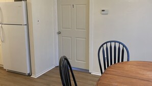 A kitchen with a white refrigerator, a dining table with chairs, and a ceiling fan with lights.