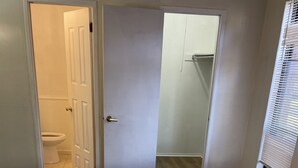 A bedroom with a bed, a door leading to a bathroom, and a window with blinds.