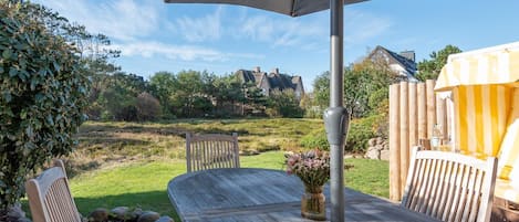 A patio with a table and chairs, a wooden fence, and a yellow-striped umbrella.