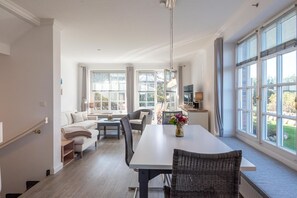 A spacious living area with a dining table, sofas, and a large window offering a view of the outdoors.