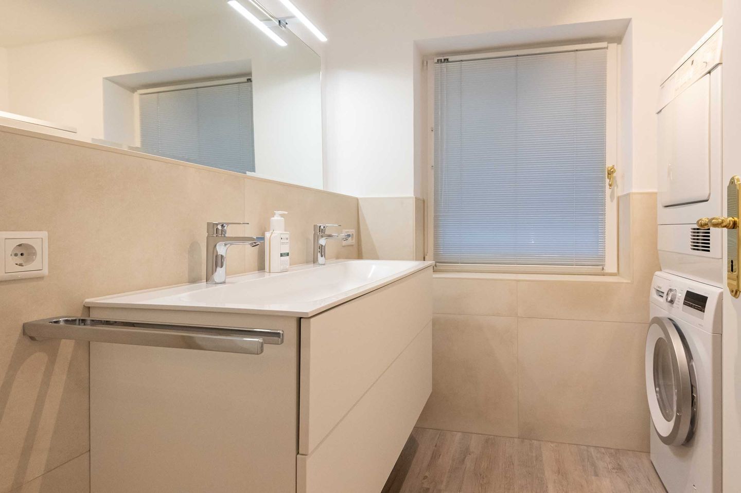A compact bathroom with a sink, mirror, window, and washing machine.