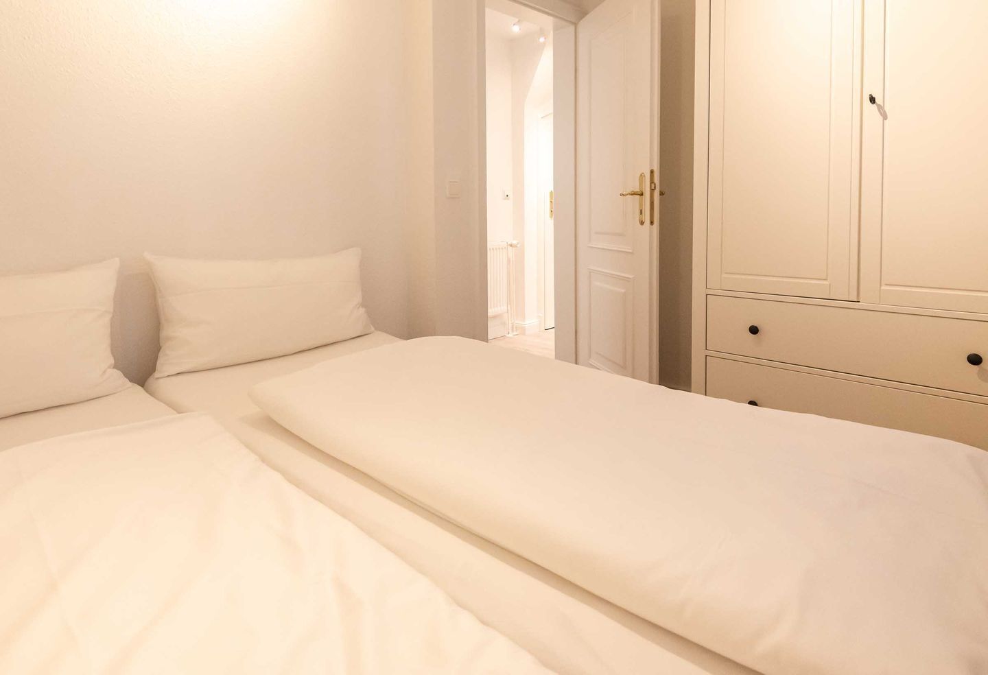 Un dormitorio con dos camas individuales, un armario y una puerta que da a otra habitación.