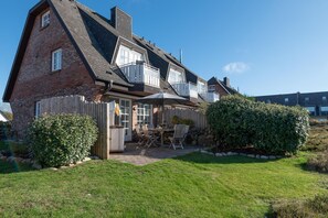 Ein zweistöckiges Haus mit Terrasse, Holzzaun und gepflegtem Rasen.