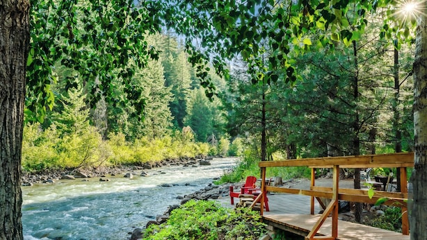A wooden deck with red chairs overlooking a river, surrounded by dense forest.