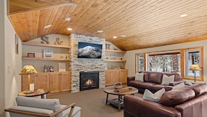 A cozy living room with a stone fireplace, leather sofas, wooden shelves, and a large window with a snowy view.