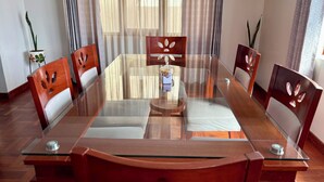 Uma área de refeições com mesa de vidro rodeada por cadeiras de madeira com detalhes recortados.