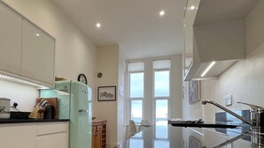 A modern kitchen with a built-in oven, a refrigerator, and a dining area with a view. - Eva's Sea View 2 Bed 2 Bath Parking & NO GUEST FEES (Broadstairs)