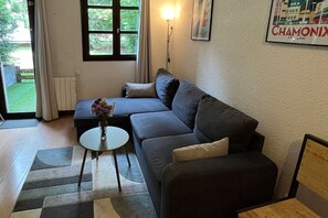 Un salon avec un canapé, une petite table sur laquelle est posé un vase, une lampe et une porte donnant sur l’extérieur.