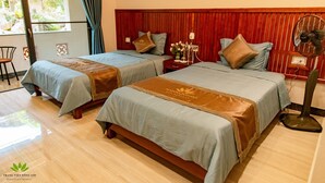 Deux lits simples avec des têtes de lit en bois, une table de chevet avec un ventilateur et une fenêtre avec des rideaux.