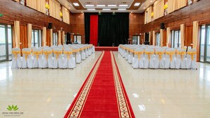 Une salle de conférence avec des rangées de chaises blanches, une moquette rouge et des panneaux de bois.