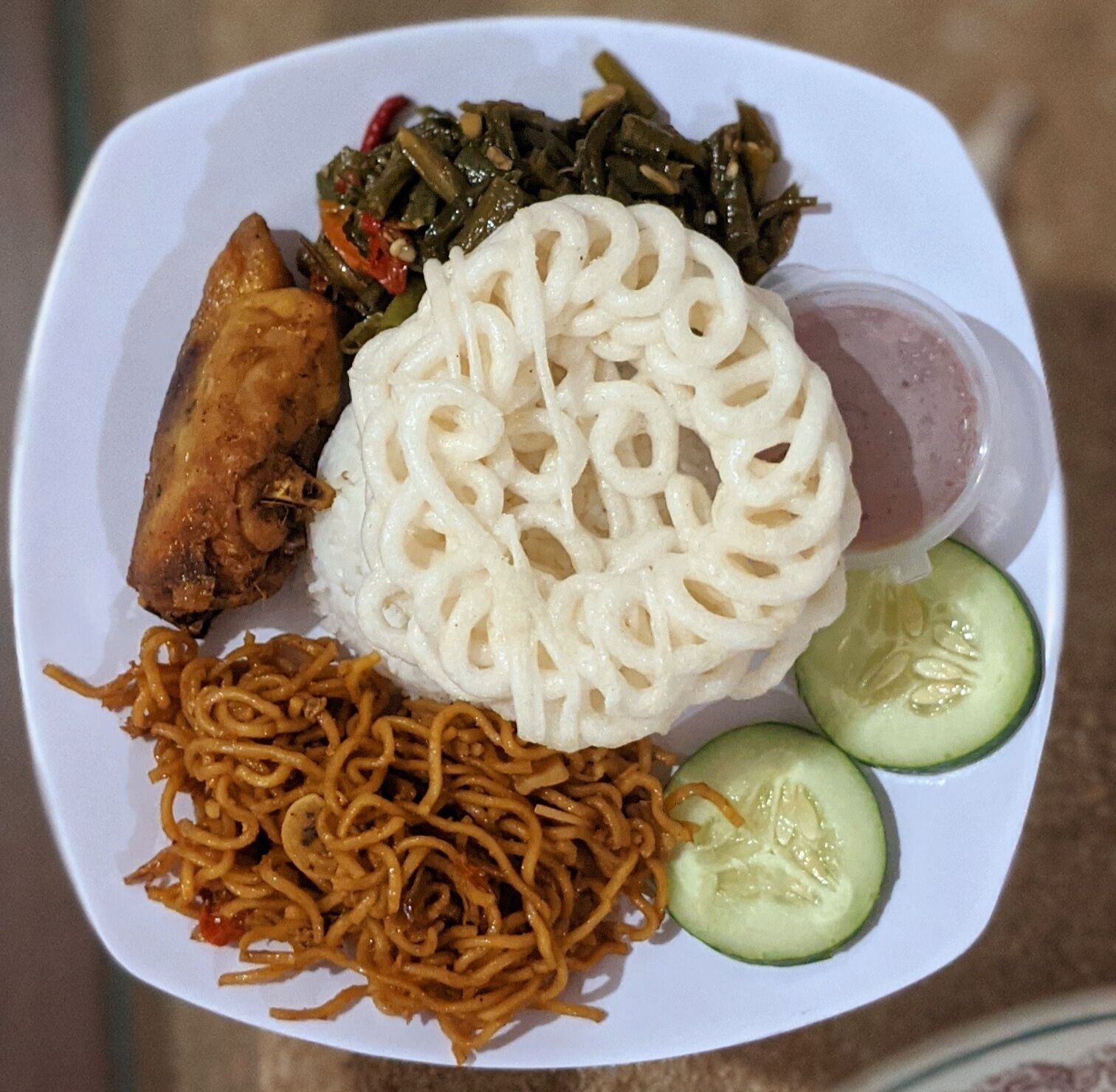 Un plato de comida con fideos, un guiso de carne, un plato de verduras y una rodaja de pepino.