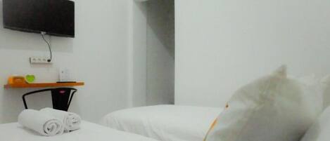A hotel room with a bed, a TV mounted on the wall, a small table with a power outlet, and a chair.