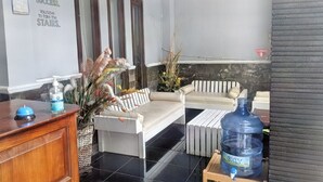 Een receptiegedeelte met een houten toonbank, een waterdispenser, een grote waterfles, een bank en een decoratieve plant.