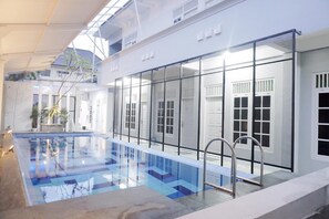 Une piscine aux carreaux bleu clair, entourée d’un bâtiment blanc doté de grandes fenêtres et de grandes portes.