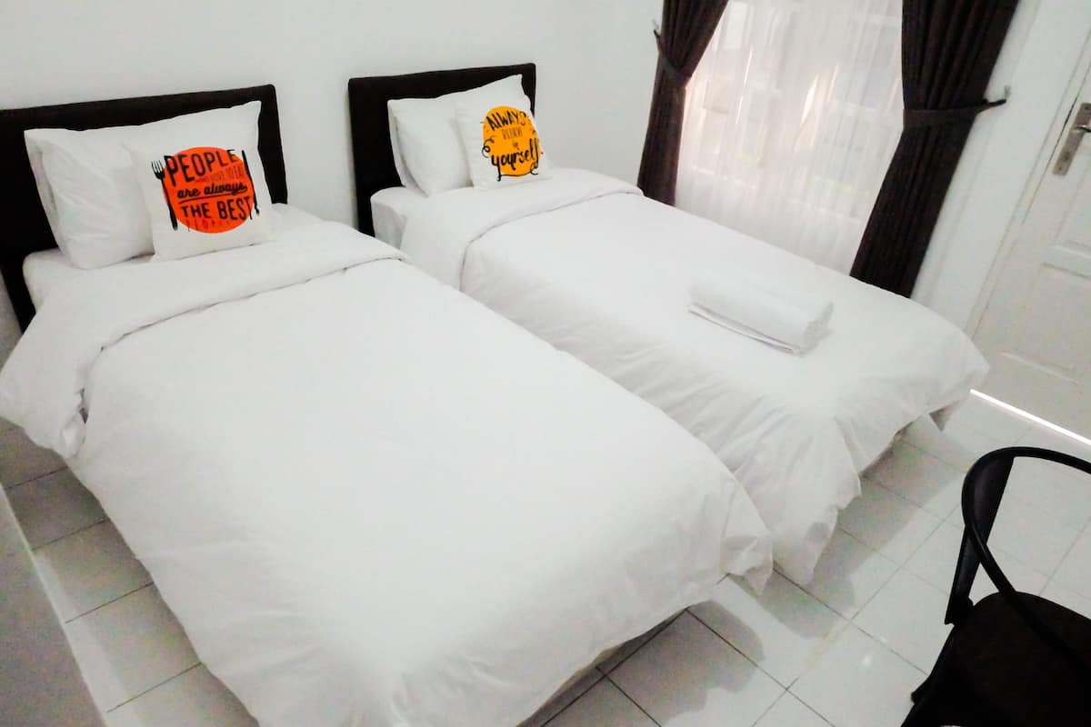 Two single beds with white bedding and pillows, a black headboard, and a white wall.