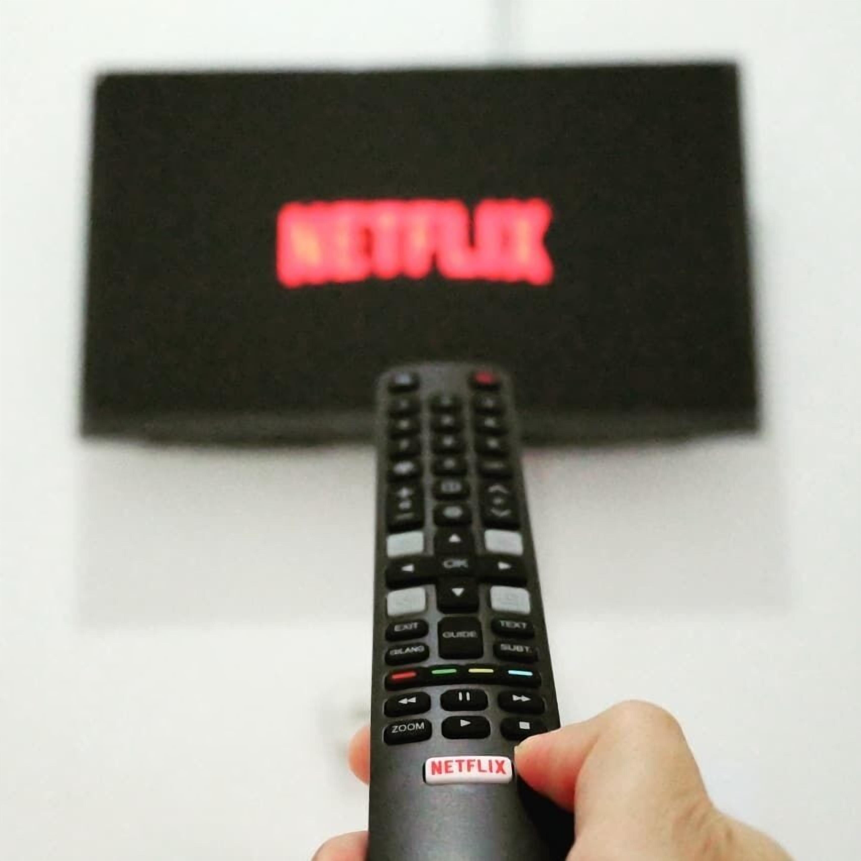 Uma mão segurando um controle remoto com o logotipo da Netflix.