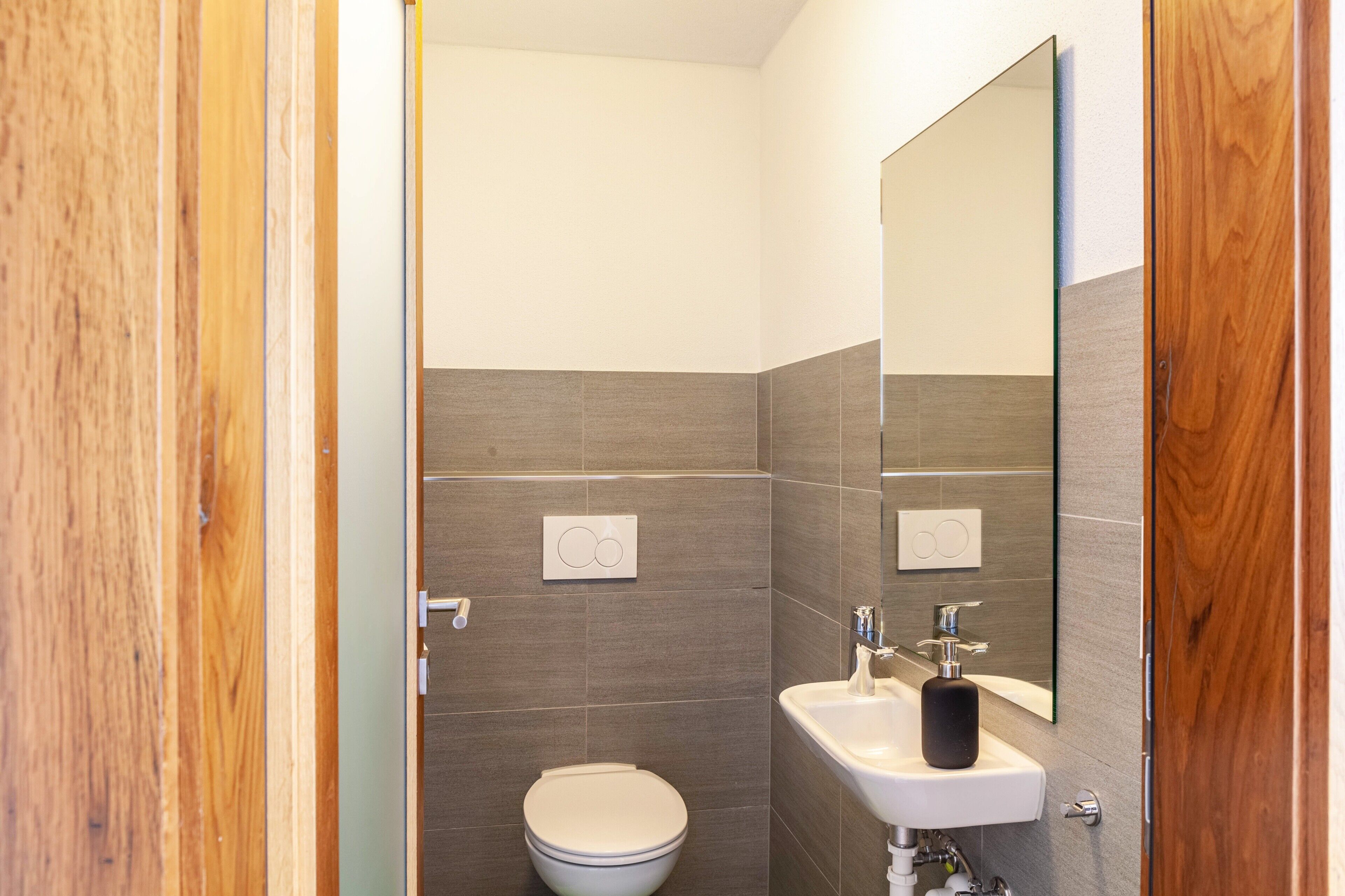 A bathroom with a toilet, sink, mirror, and wooden door.