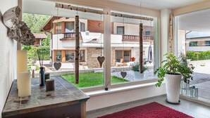 A room with a large window, a red rug, a potted plant, and a wooden swing. - Apartment "Robi" with Mountain View, Garden & Wi-Fi (Fulpmes)