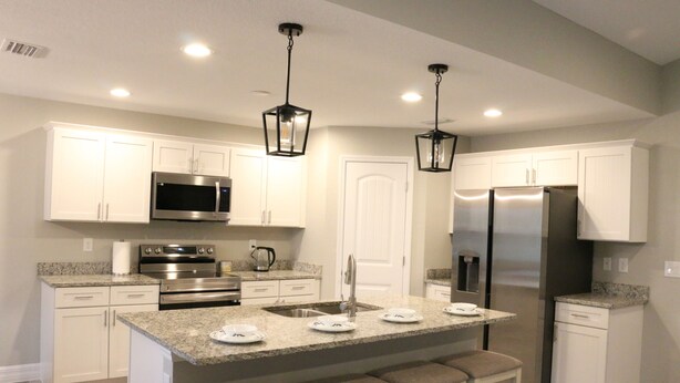 Una cocina moderna con armarios blancos, electrodomésticos de acero inoxidable, encimera de granito y una isla central con taburetes de bar.