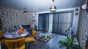A modern living room with a dining area, featuring a sofa, a coffee table, and a dining table set with blue and white plates. - Dejayz Apartment (London)