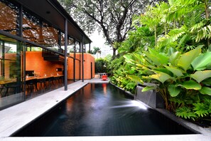 Un edificio moderno con fachada de vidrio, piscina y abundante vegetación.