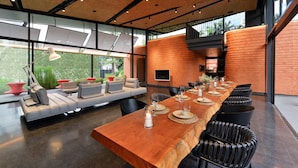 A modern dining area with a long wooden table, black chairs, and a sofa with cushions.