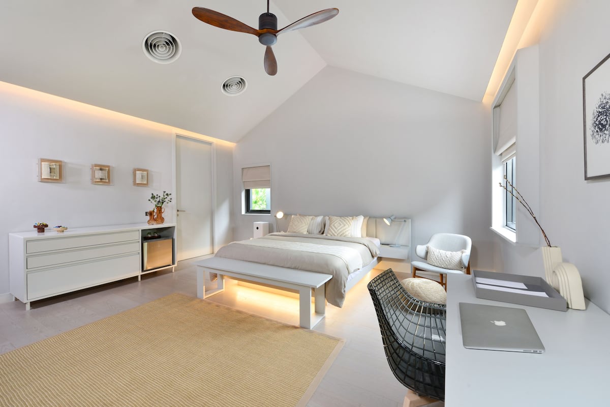 A modern bedroom with a bed, desk, chair, and ceiling fan.