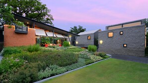 A modern building with a brick facade, large windows, and a well-maintained garden with various plants and flowers.