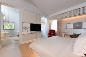 A modern bedroom with a large bed, a TV, a red chair, and a desk with a lamp.