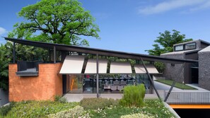 A modern building with a glass facade, a brick wall, and a large tree in the background.