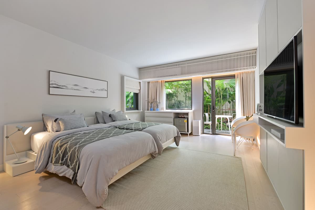 A modern bedroom with a large bed, bedside tables, a TV, and a view of greenery outside.