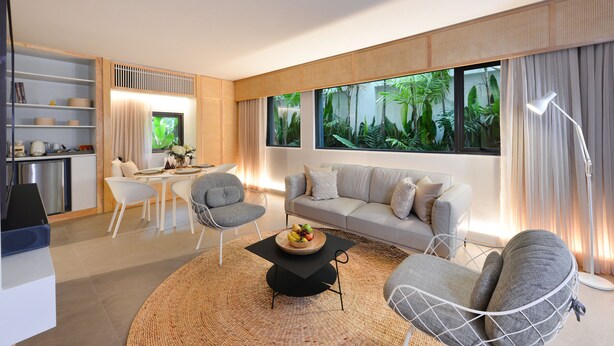 A modern living room with a sofa, chairs, a coffee table, and a kitchen area visible through an open door.