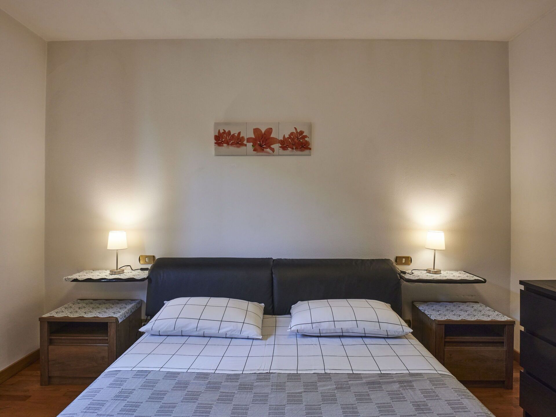 Een netjes ingerichte slaapkamer met een bed, twee nachtkastjes en een kunstwerk aan de muur.