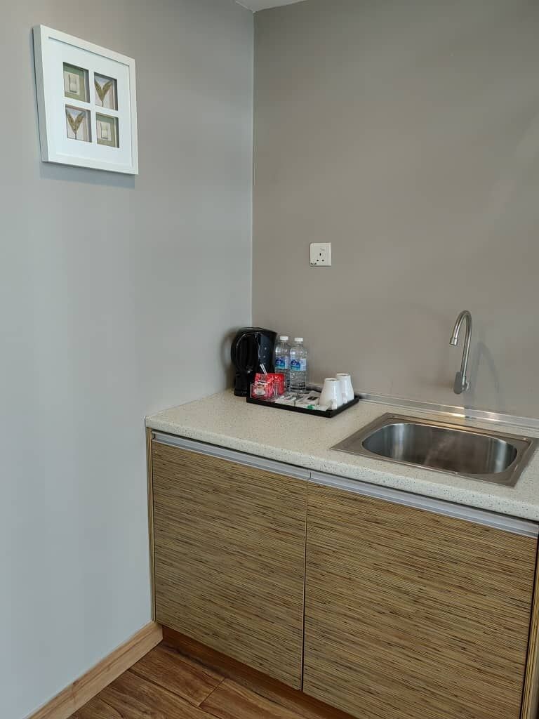 A small kitchenette with a sink, a coffee maker, and a tray with cups and bottles.
