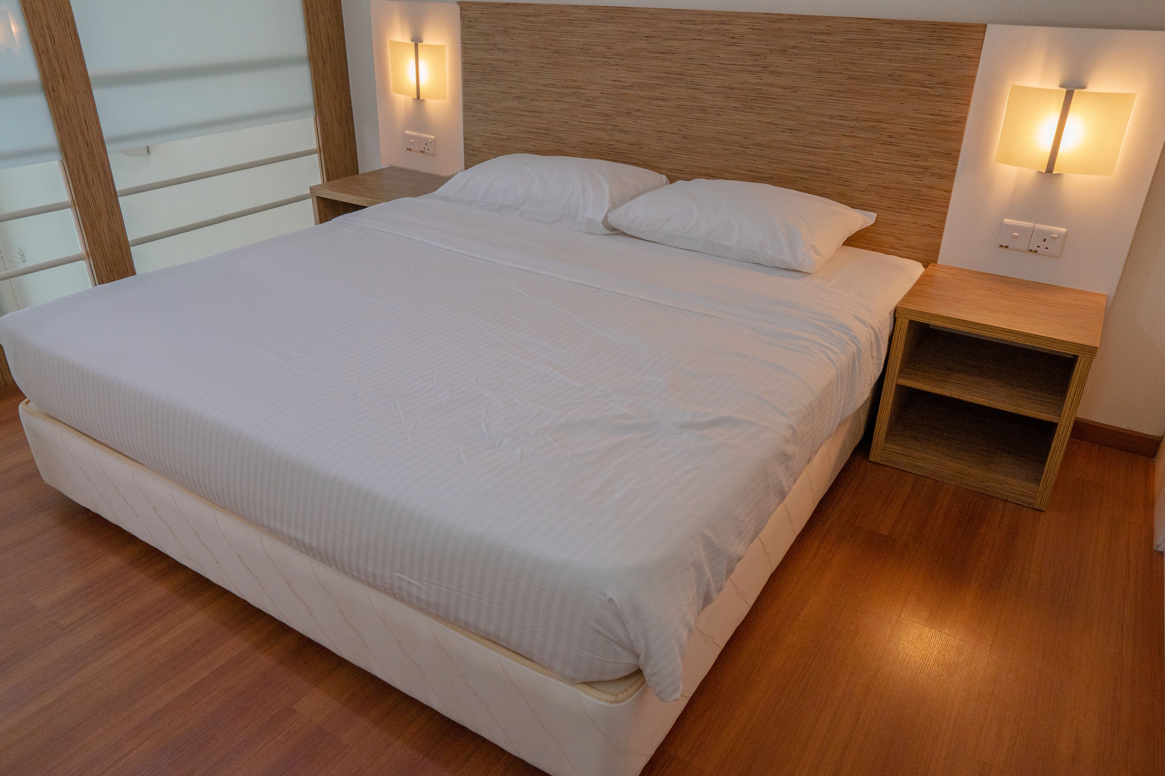 A neatly made bed with white linens, wooden headboard, and two bedside tables with wall-mounted lamps.