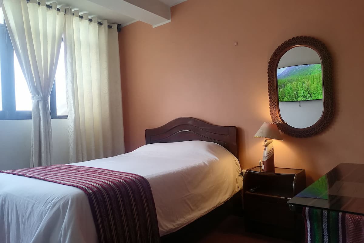 Una habitación de hotel con una cama, una mesita de noche con lámpara, un espejo y una ventana con cortinas.