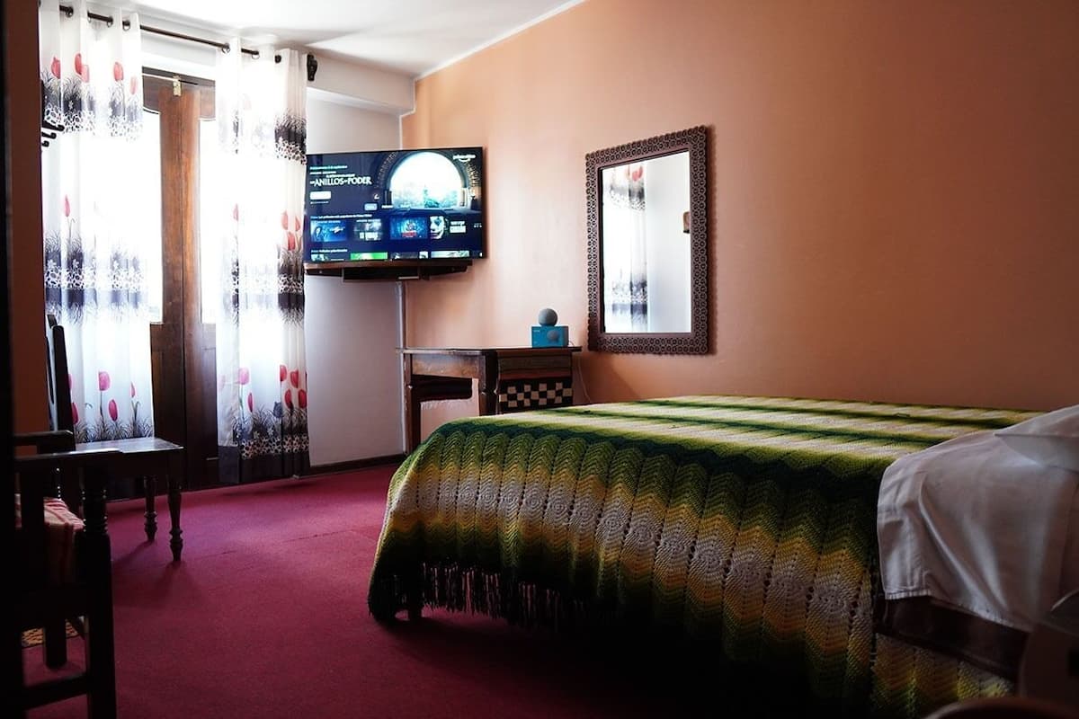Una habitación de hotel con una cama, un televisor montado en la pared, una mesita pequeña y una silla.