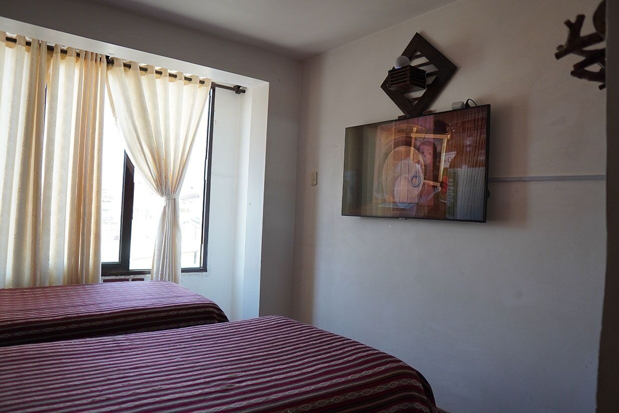 A hotel room with two beds, a window with curtains, and a wall-mounted TV.