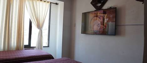 A hotel room with two beds, a window with curtains, and a wall-mounted TV.
