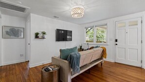 Uma sala de estar moderna com um sofá, televisão, luminária de teto e uma janela com vista para o verde.