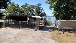 Une propriété clôturée comprenant un garage fermé, un petit bâtiment et un chalet au bord d’un lac.