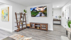 A modern living room with a wooden console table, a large landscape painting, and a ladder shelf against the wall.