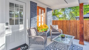 A covered porch with wicker chairs, a glass table, and a wooden fence.