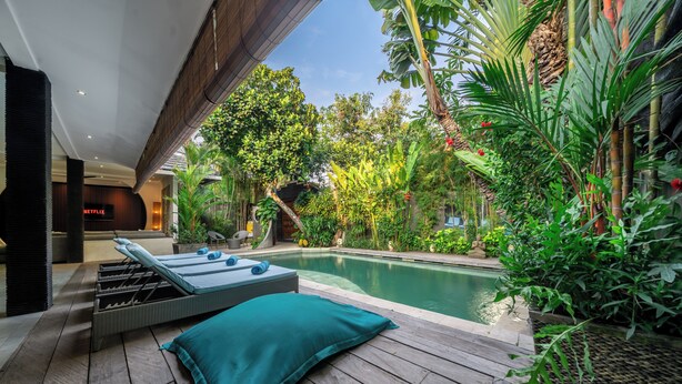 Zona de piscina amb una cadira de relax i una taula petita, envoltada de vegetació abundant i vista d'un edifici amb un rètol 'NETFLIX'.