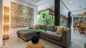 Un saló modern amb un sofà seccional, una paret decorativa i una zona de menjador amb mobiliari de vimet.