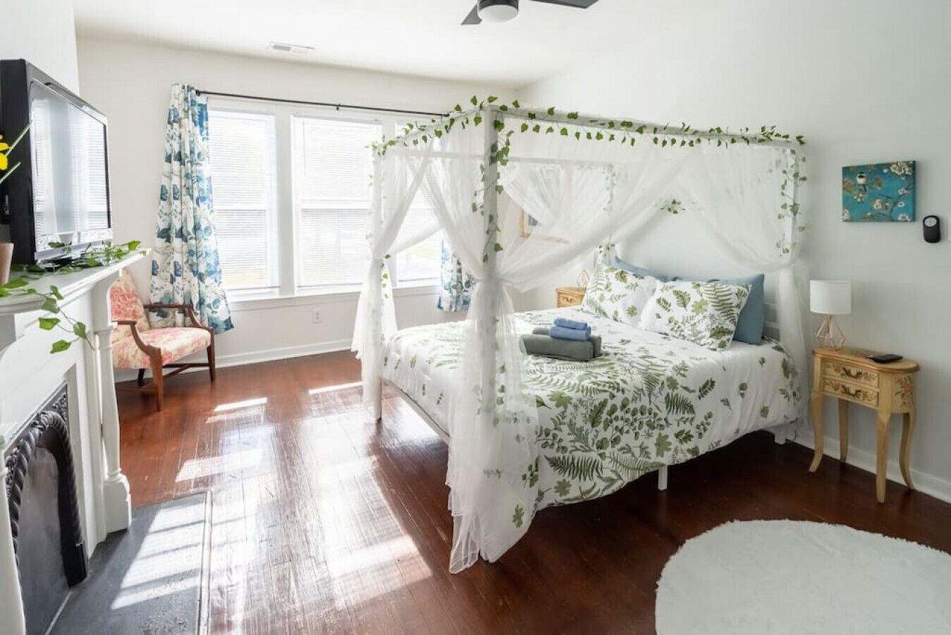 A romantic queen canopy bed invites you to relax, complemented by a Smart TV, ceiling fan, dresser drawers, and ample natural light for a serene, enchanting retreat.
