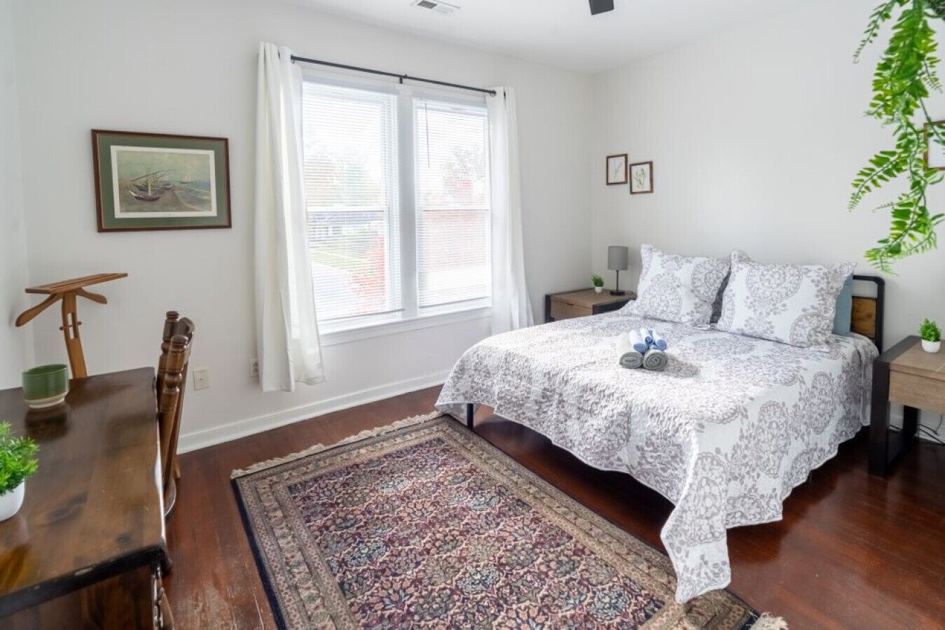Une chambre à coucher avec un lit, une table de chevet, une chaise, une fenêtre avec des stores et un tapis.